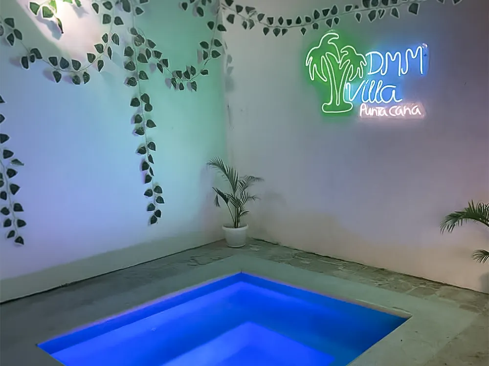 The jacuzzi lit blue at night beneath the villa's neon sign